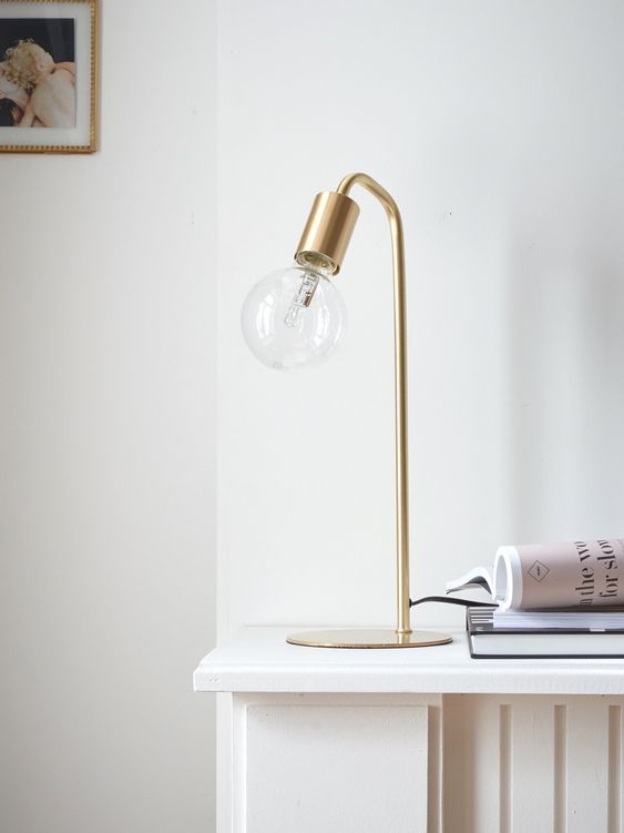 Une lampe de bureau en laiton dorée avec une grosse ampoule ronde à découvert. 